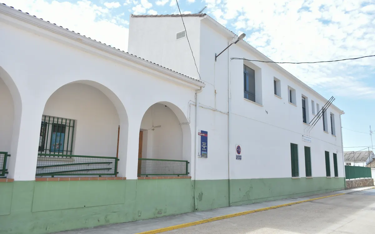 Fachada blanca de un colegio rural con arcos y zócalo verde en Toledo